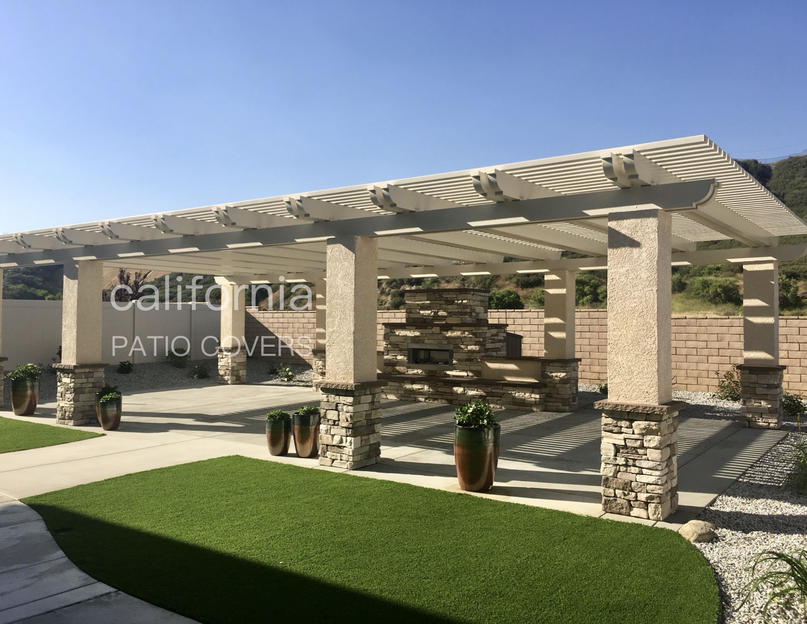 Modern patio cover with a stone feature wall, shaded area, and landscaped greenery, showcasing outdoor living space design options.