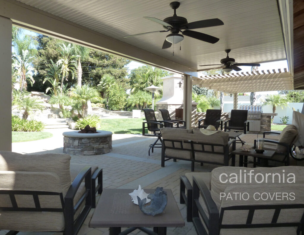 Stylish outdoor patio with seating, ceiling fans, and a stone fire pit, surrounded by lush greenery, ideal for relaxation and entertainment.