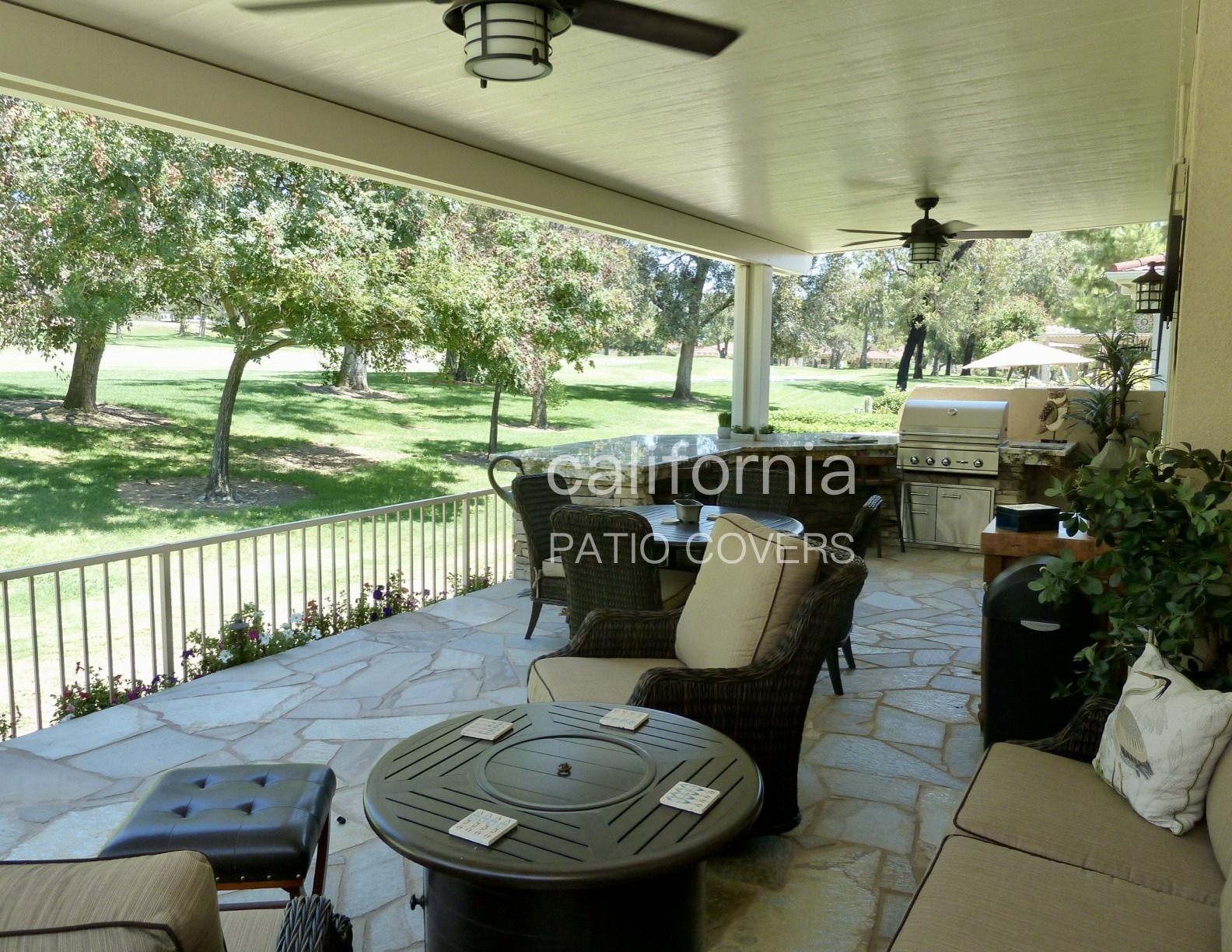 Covered patio featuring two ceiling fans, with a view of lush green trees and a golf course in the background, enhancing outdoor relaxation.